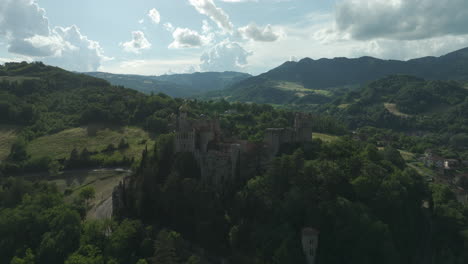 a medieval castle surrounded by lush green hills under a partly cloudy sky, aerial view