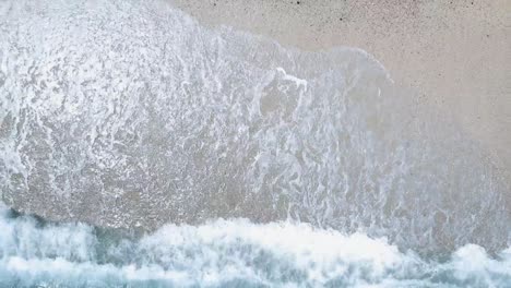 drone ascending over waves of the ocean breaking on a white pebble beach