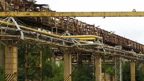 exterior view of abandoned soviet heavy metallurgy melting factory liepajas metalurgs territory, rust-covered heat pipelines on concrete poles, overcast day, medium shot