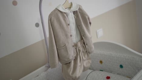 neutral toned baby clothes hang neatly above a cushioned crib in a cozy modern nursery