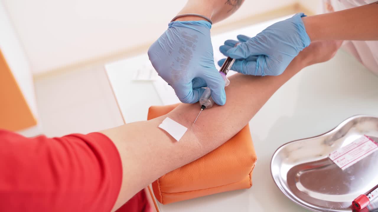 Process of taking a blood sample from vein. Hands of a nurse in blue gloves pricking a needle into a patient's vein. Medical assistant collecting blood from vein. Close-up.