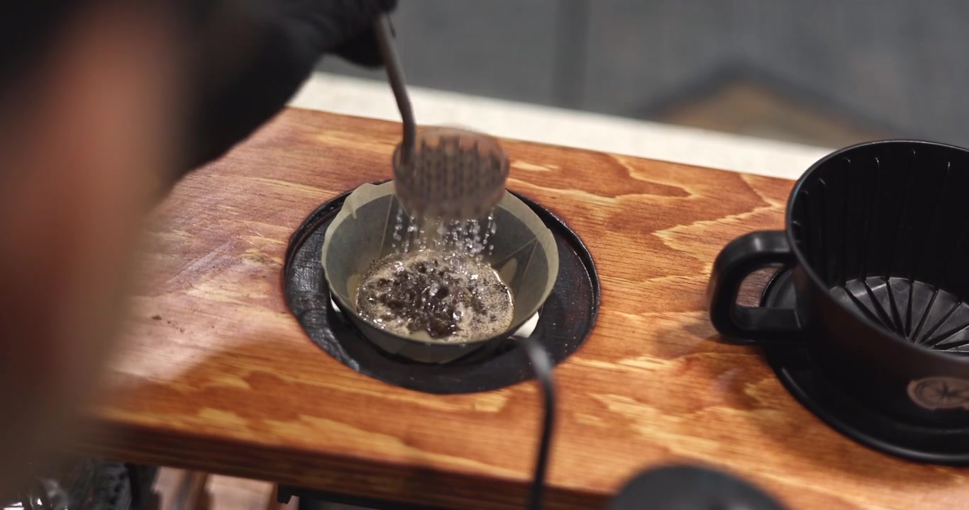 Barista continues blooming coffee with a dispersion screen during manual pour over brewing, overhead slow motion orbit