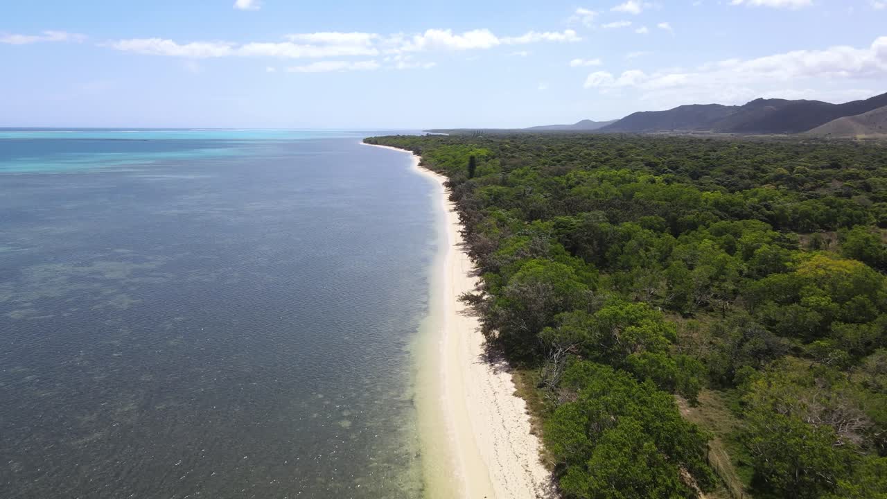 Drone aerial moving forward over a beach with a mountainscape in New Caledonia