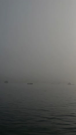 Minimalist seascape featuring small boats gliding through fog on a tranquil lake, surrounded by calm water under a gray, overcast sky, creating a serene and ethereal atmosphere