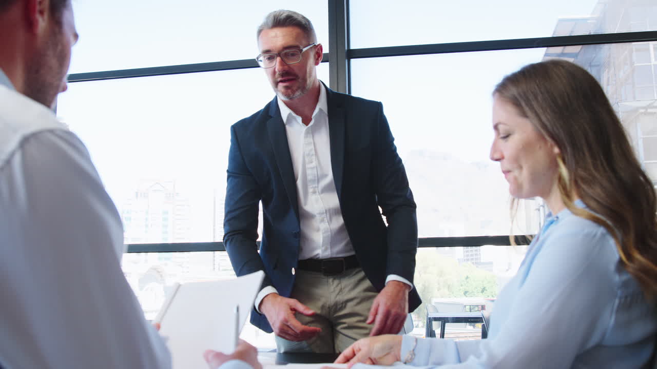 Business Team Meeting Around Office Boardroom Table With Laptops Discussing Documents