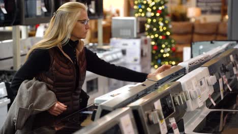 mujer rubia bastante madura comprando una estufa en una sala de exposición de una tienda de electrodomésticos de cocina