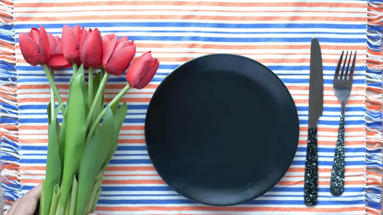 Piatto vuoto con tulipani e posate su una tovaglia a righe