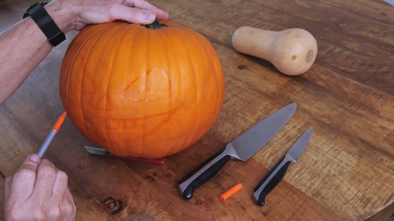 Person sketching jack-o’-lantern design on pumpkin with orange pen
