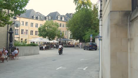 Pedestrians and diners enjoy outdoor seating along a tree-lined street with shops and restaurants