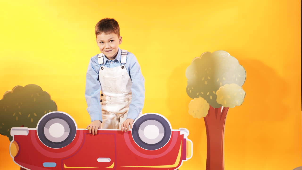 Little boy with a bright red car on a yellow background in the studio. Happy children.