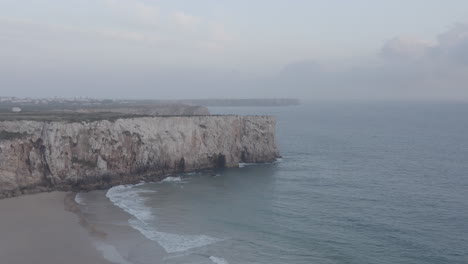 Breathtaking-aerial-drone-view-of-Lagos-Algarve-rocky-cliff-coastline,-waves-crashing-against-shore,-sideway-flight,-Portugal,-day