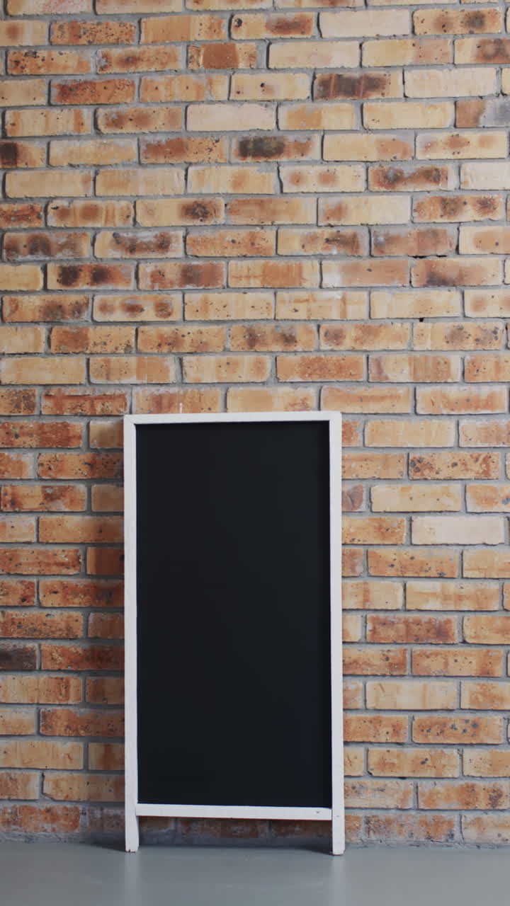Vertical video of blackboard sign on white stand with copy space on brick wall background