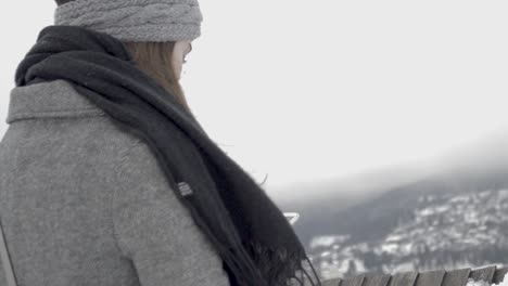 from behind shot of a girl with a black scarf and grey coat looking at and playing with her smartphone, slomo