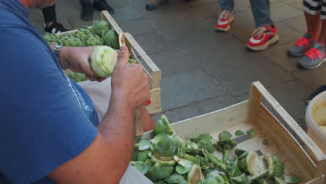 male person cutting and peeling fresh artichoke outdoors on food market during tourists watching. venice,italy