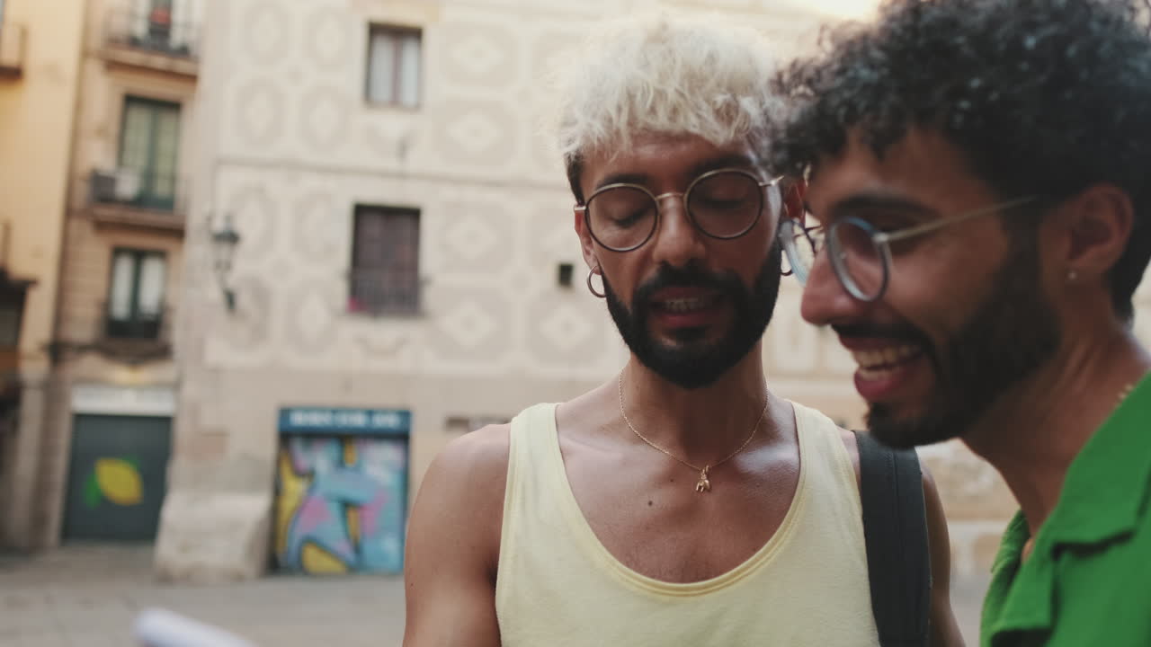 Two Young Men Talking and Looking at a Smartphone on a City Street