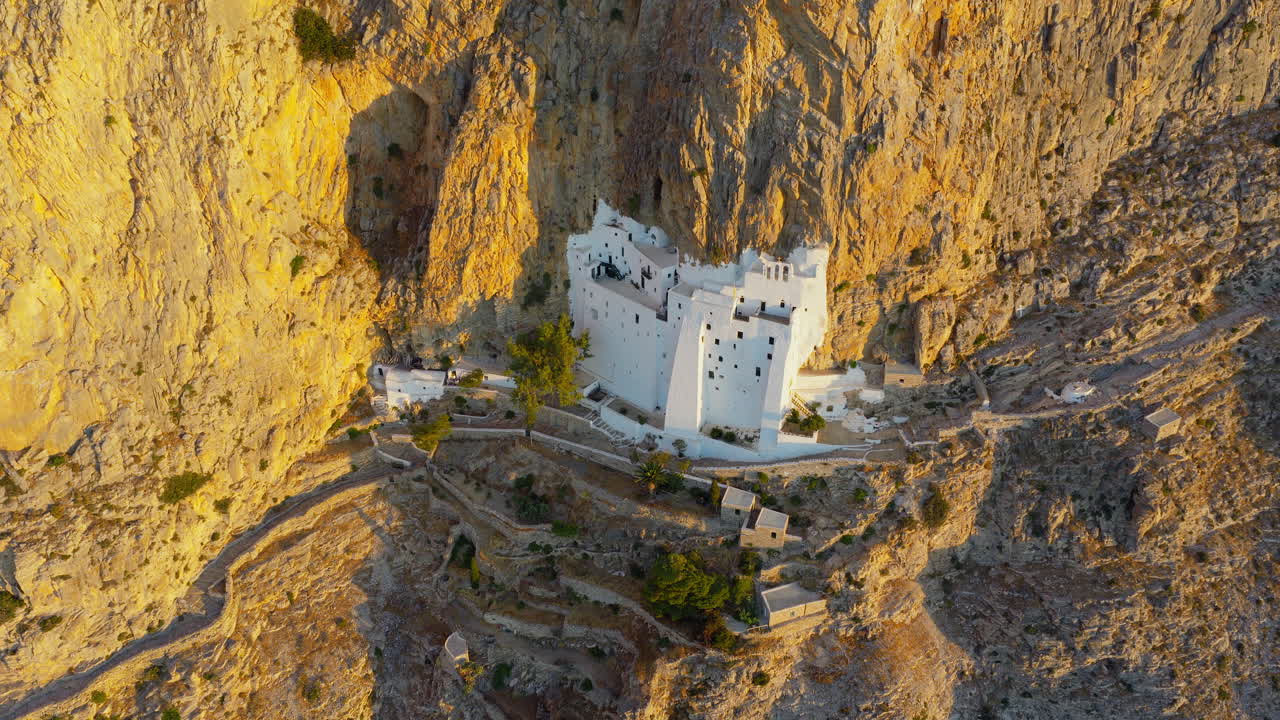 The Panagia Hozoviotissa Monastery on steep cliffside above sea at golden hour sunlight, Amorgos Island, Aerial revealing shot