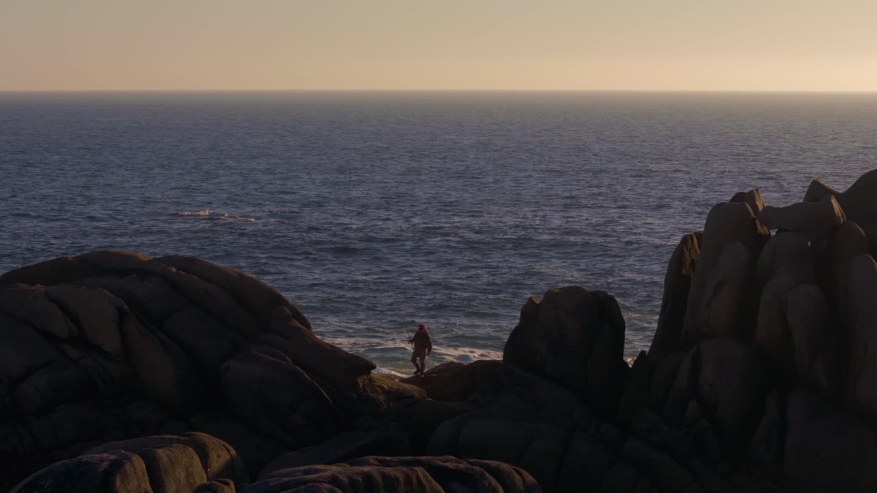 Person Standing On The Rock, Fishing In The Sea At Sunset. - wide shot