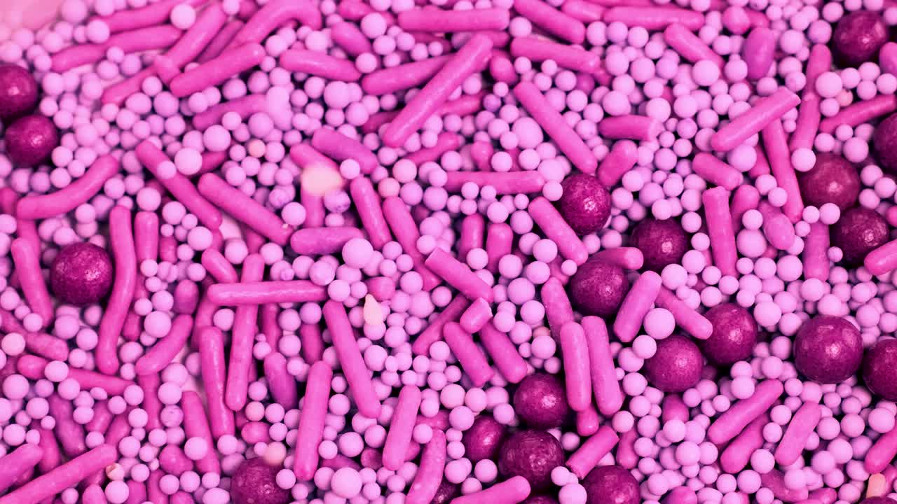 Macro view of pink candy sprinkles cascading onto a surface, creating a dynamic, colorful pattern