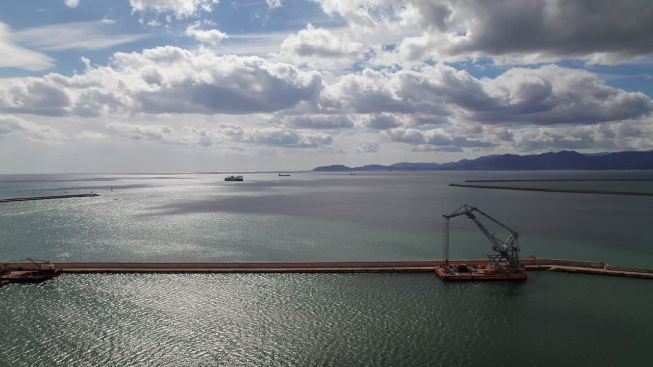 Aerial shot of Mediterranean Sea in Sardinia, Italy. Gorgeous sunny day with clouds and mountains, harbor breakwater in foreground.