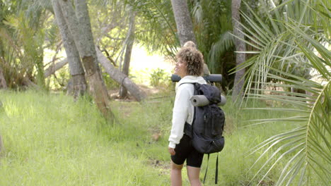 young biracial woman with curly hair carries a backpack in a lush forest with copy space