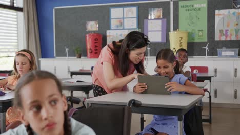 Feliz-Y-Diversa-Maestra-Ayudando-A-Una-Niña-Usando-Una-Tableta-En-Clase-De-Escuela-Primaria,-Cámara-Lenta