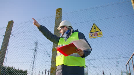 male engineer holding clipboard and pointing directions while dictating instructions, handheld dynamic