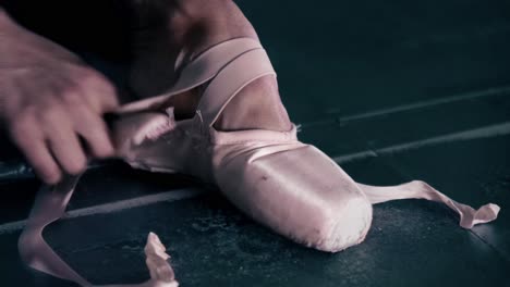 ballerina puts on ballet shoes in a dark studio room