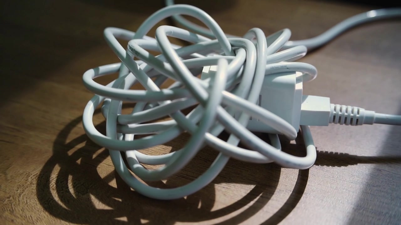 Camera shifting, tangled white USB cable opening on wood desk, showing shadow rings and adapter