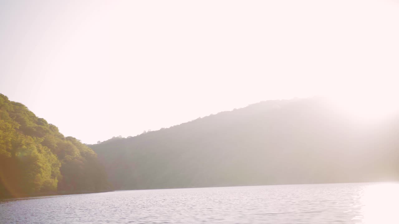 Beautiful smooth lake water, point of view from the front of a speed boat, with green mountains at sunset with flares