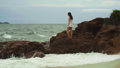 joven morena que se queda en las rocas cerca del mar en un clima tormentoso