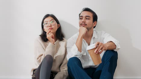 a couple in love are sitting by wall in new apartment, they are looking around room thinking deeply about choice of decoration, furnishing the house, drinking coffee from takeaway cups