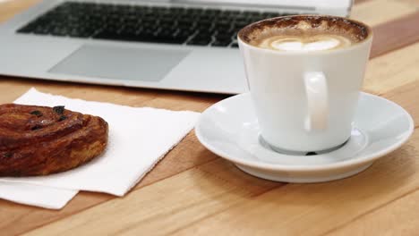 primer plano de una computadora portátil con una taza de café y una galleta dulce