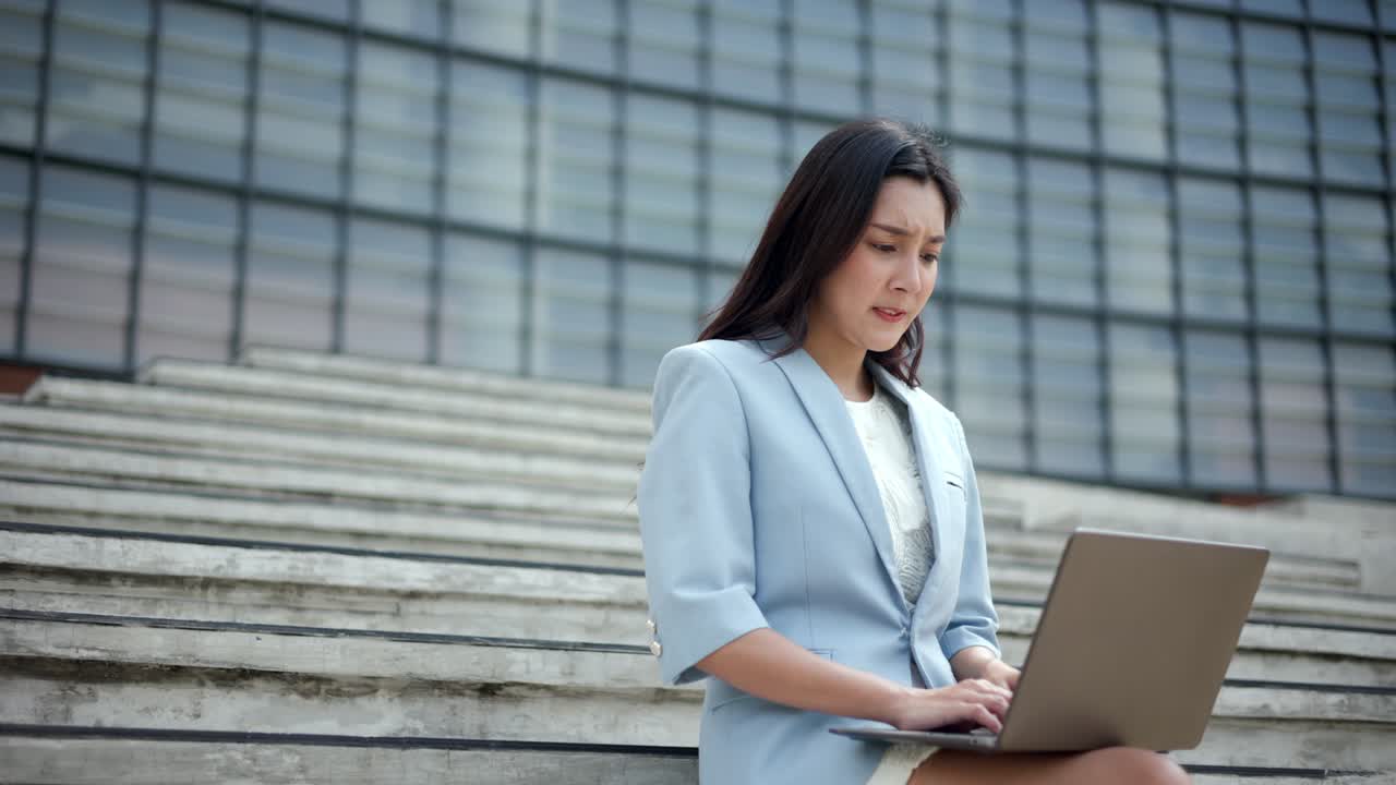 도심의 사무실 건물 근처의 계단에서 노트북에서 일하는 심각한 사업가 여성. 온라인 회의에 노트북을 사용하는 불행한 여성.