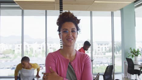 Portrait-of-smiling-biracial-creative-businesswoman-in-office-with-diverse-colleagues-in-background