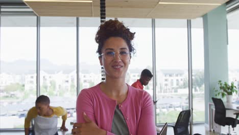 portrait of smiling biracial creative businesswoman in office with diverse colleagues in background