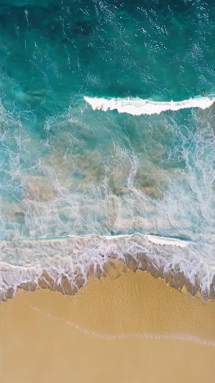Aerial view of turquoise waves gently lapping a sandy beach, creating a serene and calming video