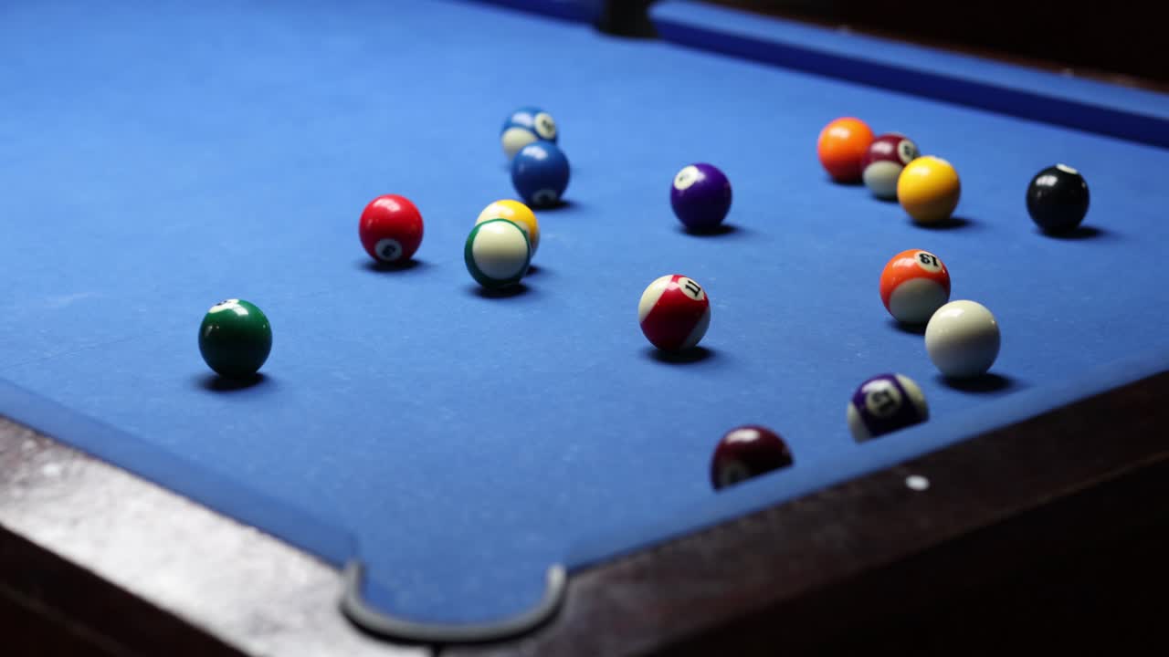 Speler stoot kleurrijke ballen in een driehoekrek op een biljart.