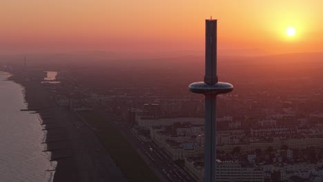 drone orbit of brighton’s i360 tower during golden hour, showcasing warm light, the cityscape in the background, and the modern coastal architecture