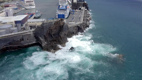 static drone shoot of waves splicing agains rocks near cruise terminal in funchal, madeira at back of fort saint joseph