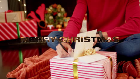 animation of happy holidays text over caucasian man writing christmas cards with presents