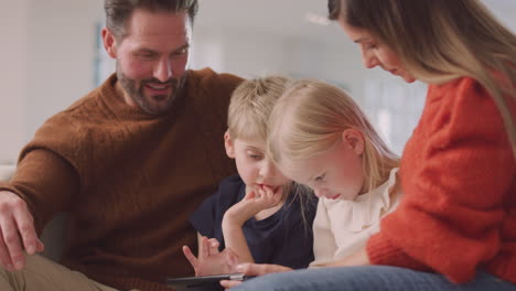 lächelnde familie sitzt auf dem sofa und hat spaß, indem sie zusammen ein digitales tablet benutzt
