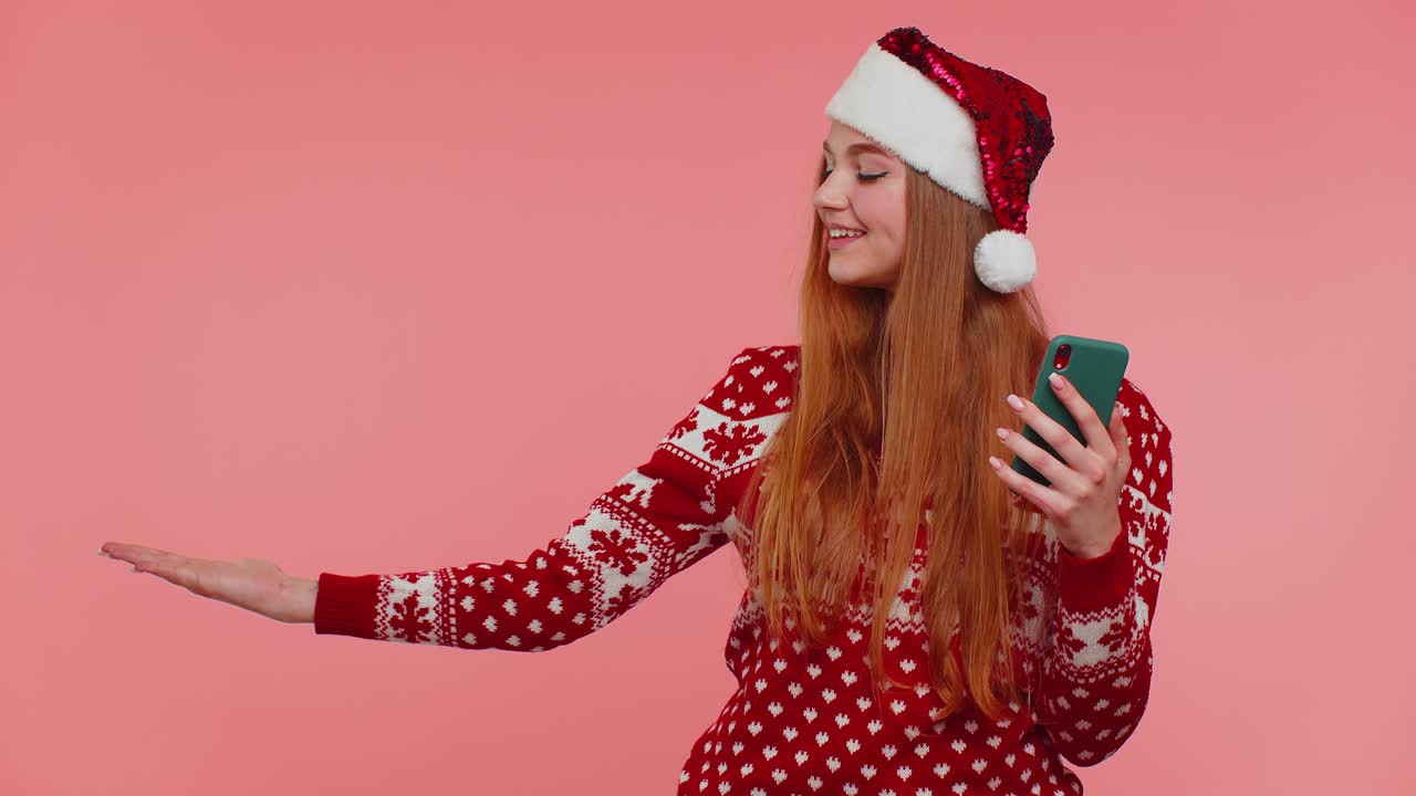 Girl in christmas santa sweater with mobile phone showing pointing empty place advertising area
