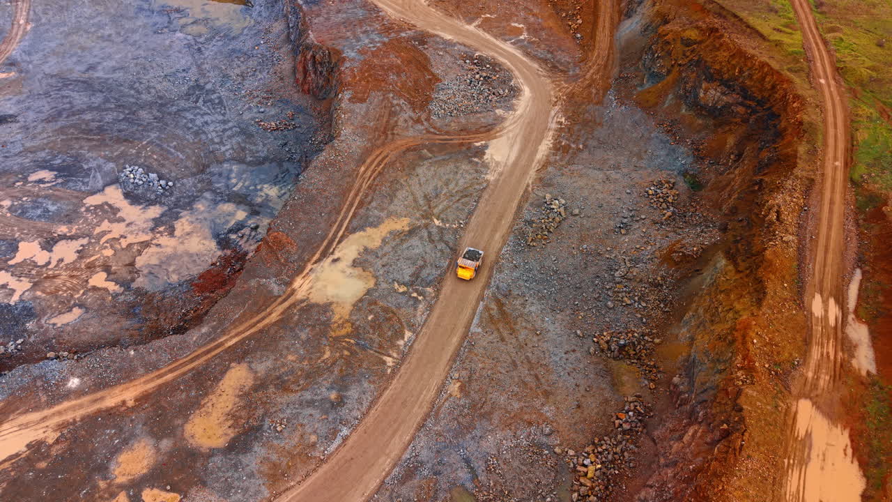 Yellow truck on dirt road. A yellow truck moves along a dirt road in a quarry surrounded by rocky terrain and machinery. It is a sunny day