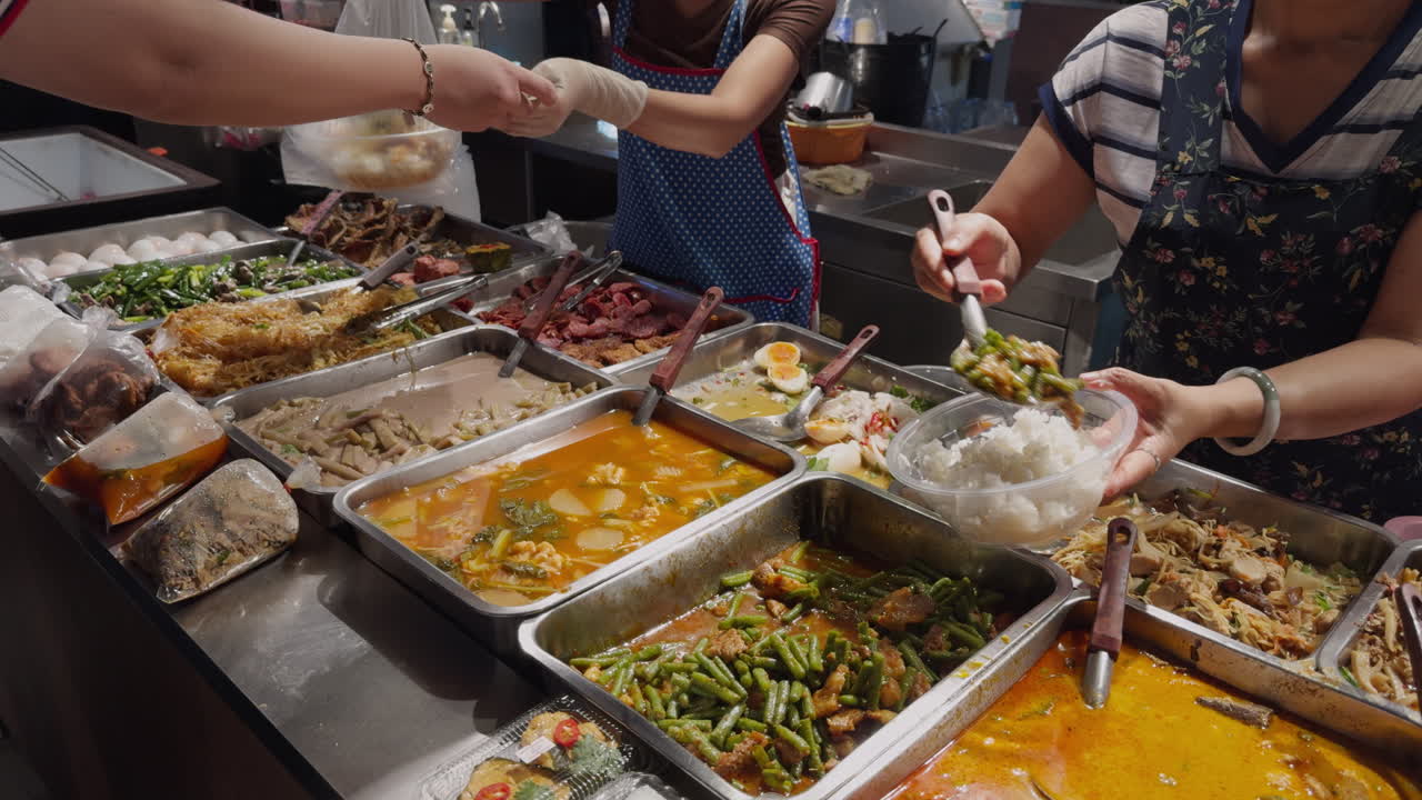 Venditore di cibo da strada thailandese che serve piatti a buffet, prelevando cibo e consegnando il pasto a un cliente in un vivace mercato locale. Autentico cibo da strada asiatico e scena di vita quotidiana