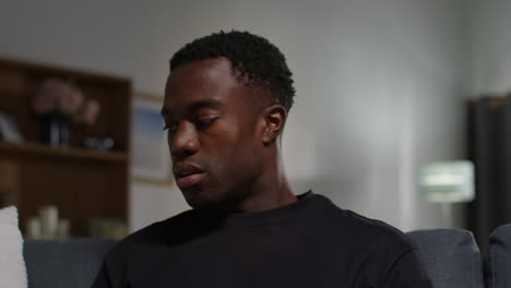 unhappy and depressed young man sitting on sofa at home ending call after talking on mobile phone shaking head