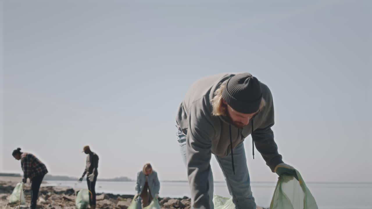 Man Collecting Garbage on Shore with Environmental Activists