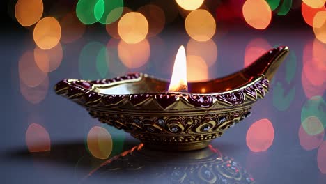 close-up video of a decorative oil lamp with a lit flame, set against a vibrant bokeh background