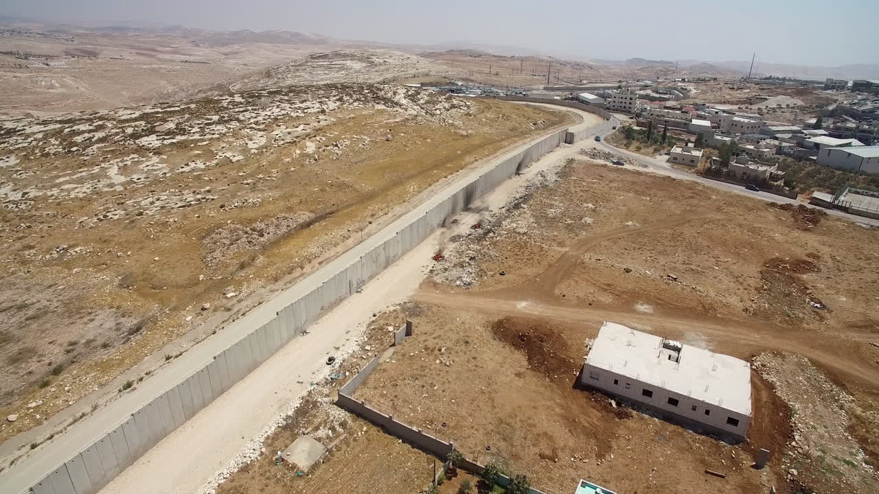 Aerial View of a Concrete Separation Barrier in a Dry, Hilly Landscape Adjacent to a Village