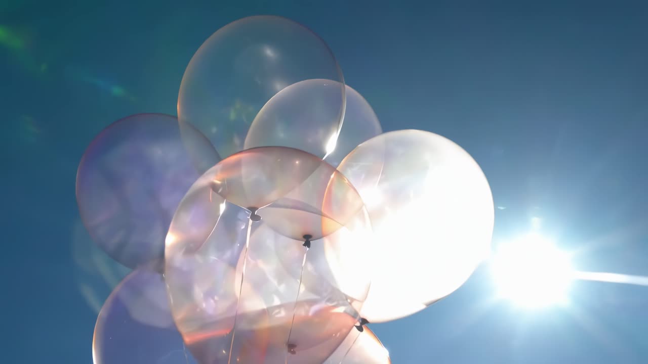 光と色彩を捉えた、澄み切った青空を背景にした半透明の風船のローアングル映像。