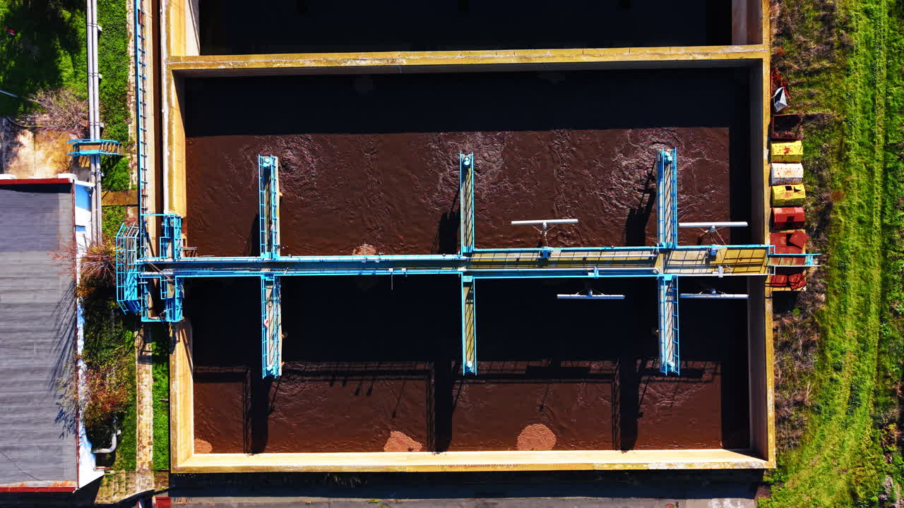 Directly above aerial view of a large rectangular wastewater tank with active aeration process, blue metal bridges, and mechanical equipment